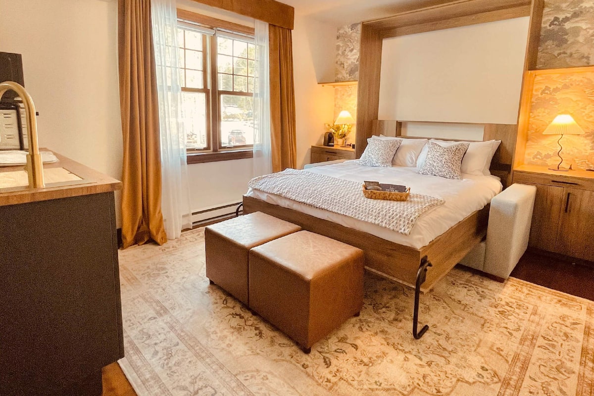 A neatly arranged bedroom with a large bed, bedside tables, a desk, and a window with curtains.