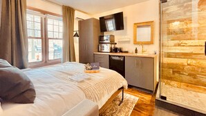 A bedroom with a bed, a small kitchenette, a television, and a sliding glass door to a balcony. - Estello Suites et Spa (Frontenac)