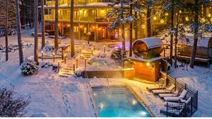 A large, multi-story wooden lodge with a swimming pool surrounded by snow, illuminated by warm lights. - Estello Suites et Spa (Frontenac)