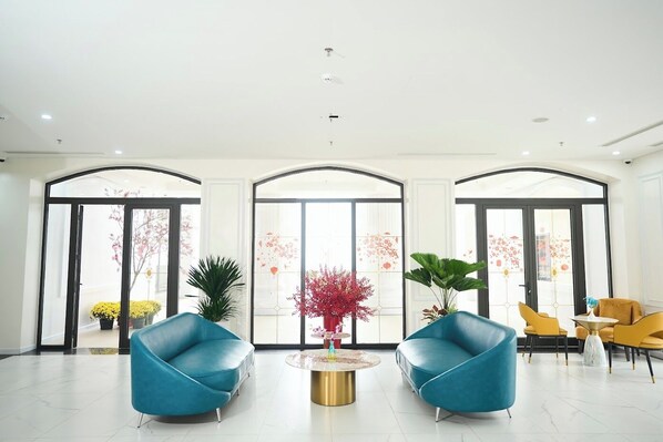 A spacious lobby with a modern design, featuring two blue armchairs, a round coffee table, and a large window with a view of the outside. - Belliss Hotel And Spa (Xuan Hoa)