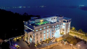 Un grande edificio a più piani con piscina sul tetto, circondato da un’area di parcheggio ben illuminata e vista sul mare.