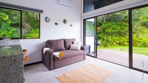 Een moderne woonkamer met een grijze bank, een salontafel en een grote schuifpui die uitkomt op een houten terras.