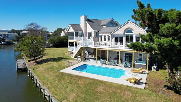 Uma casa de dois andares com um deck amplo, piscina e um píer que se estende sobre a água.
