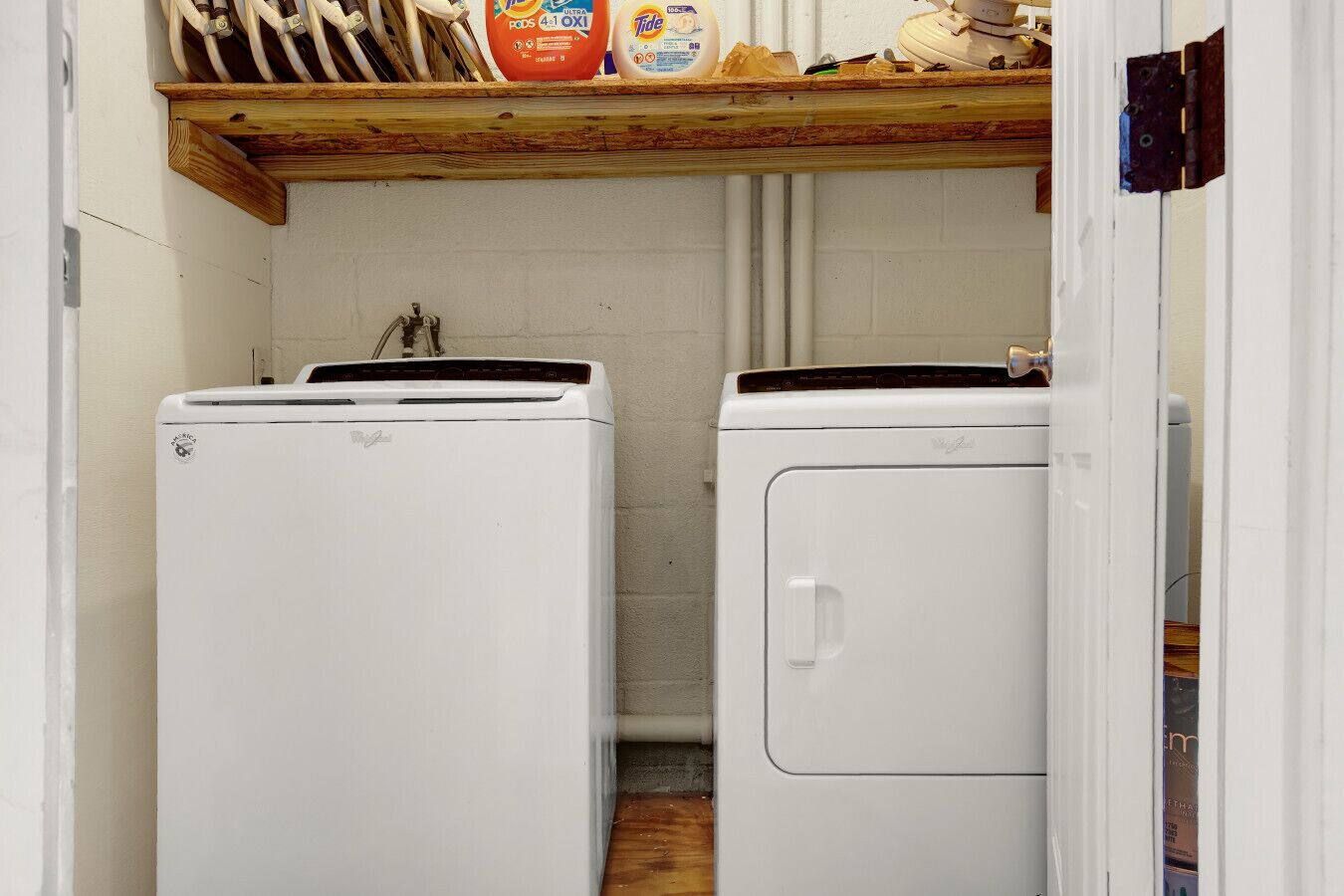 A laundry room with two white washing machines, a shelf with cleaning supplies, and a wooden beam above.