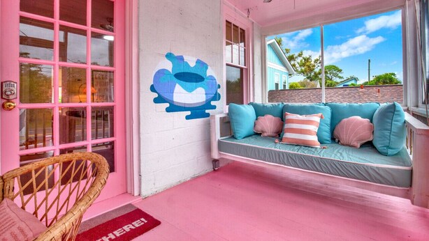 A pink-themed room with a large window, a wall mural, and a sofa with cushions. - 4 BDR Heated Pool, Professionally Designed Vacation Rental Across from Beach (Tybee Island)