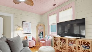 A cozy living room with a grey sofa, pink armchairs, a TV, and a wooden cabinet. - 4 BDR Heated Pool, Professionally Designed Vacation Rental Across from Beach (Tybee Island)
