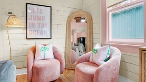A room with two pink armchairs, a framed motivational quote, a large mirror, and a lamp. - 4 BDR Heated Pool, Professionally Designed Vacation Rental Across from Beach (Tybee Island)