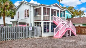 A two-story building with a pink staircase and a wooden fence. - 4 BDR Heated Pool, Professionally Designed Vacation Rental Across from Beach (Tybee Island)