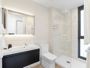 Um banheiro moderno com chuveiro em cabine de vidro, pia branca e armário preto.
