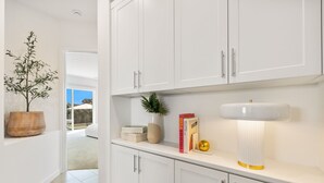Een moderne keuken met witte kasten, een wit aanrecht, een bloempot, een vaas en een lamp.