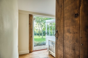 A room with a wooden door leading to a balcony with a view of a garden.