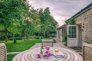 A patio with a round table, chairs, and a door to a stone building.