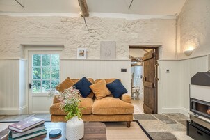 A cozy living room with a stone wall, a wooden door, a fireplace, and a window with a view of greenery.