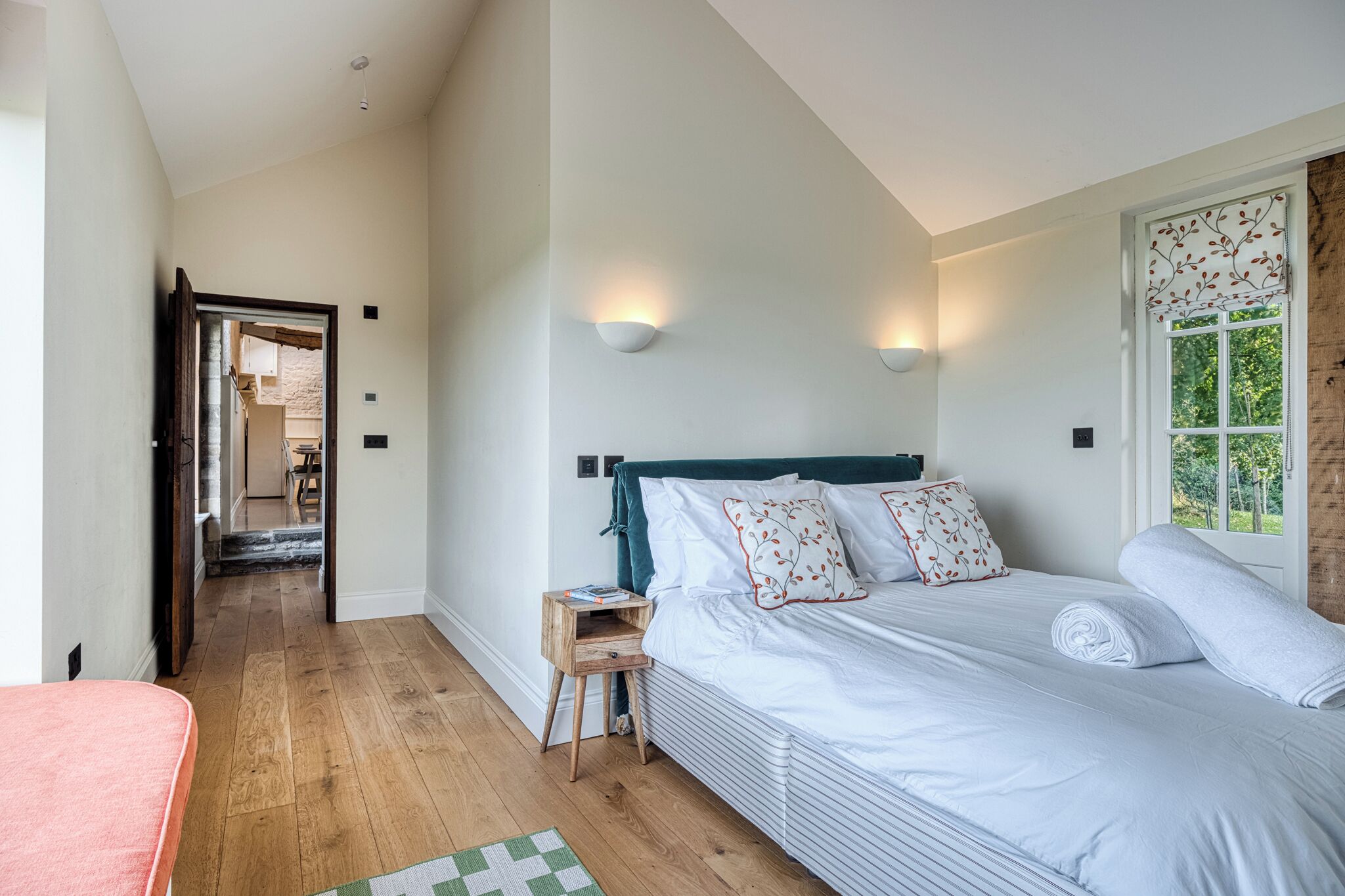 A bedroom with a bed, bedside table, and a view of the outdoors.