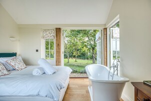 A bedroom with a large bed, a bathtub, and a view of a garden.