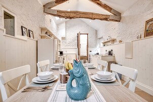 A dining area with a high ceiling and exposed beams, white walls, and a large fish-shaped vase on the table.