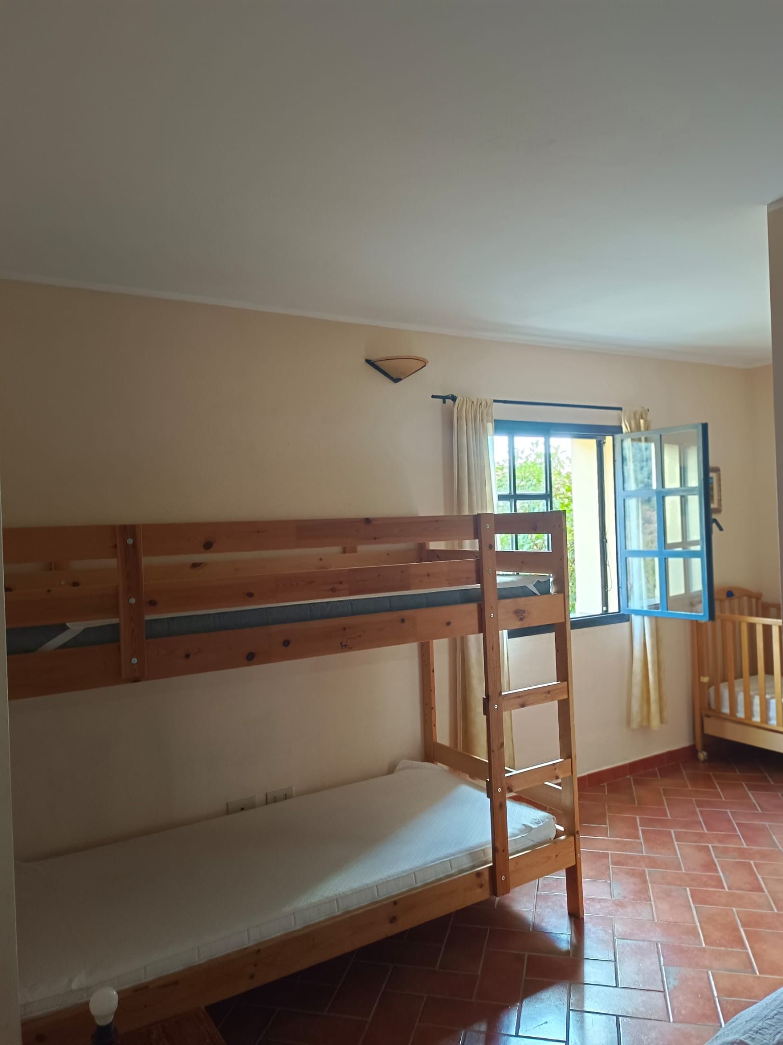 Une chambre avec un lit superposé, une fenêtre avec des rideaux et une porte dotée d’un cadre bleu.