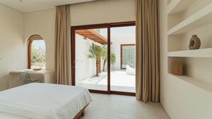 A bedroom with a bed, a desk, and a view of a courtyard. - Villa Sari 2 by Alfred in Bali (Pecatu)