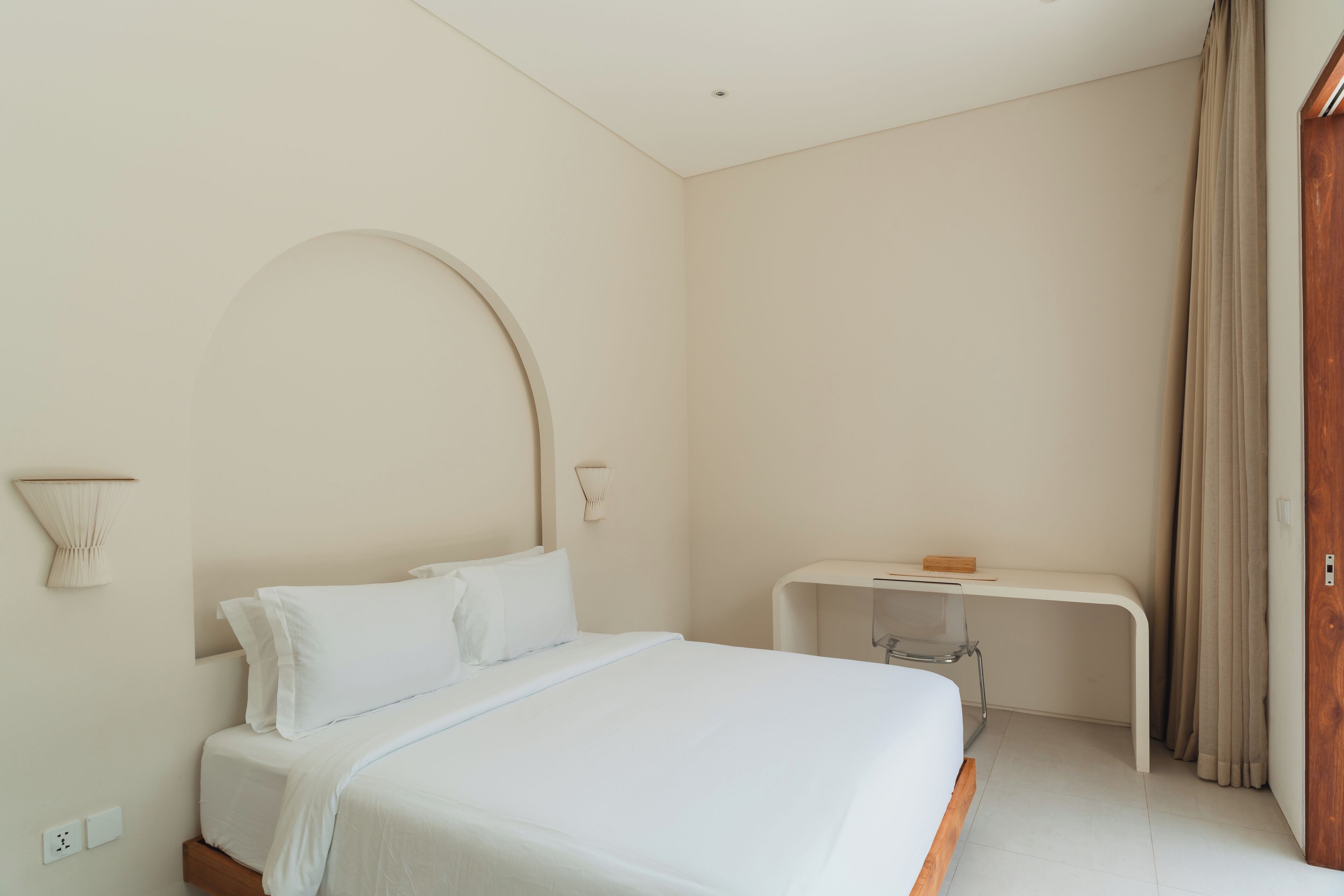 Camera d'albergo minimalista con un letto, una scrivania e una porta in legno.