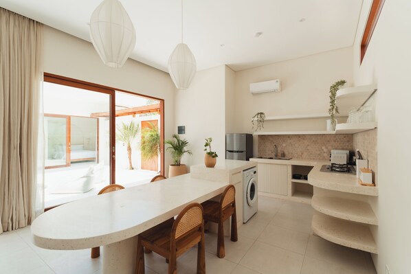 A modern kitchen with a central island, built-in appliances, and a view to a balcony. - Villa Sari 2 by Alfred in Bali (Pecatu)