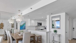 Una cocina moderna con armarios blancos, una isla central y un comedor con sillas blancas.
