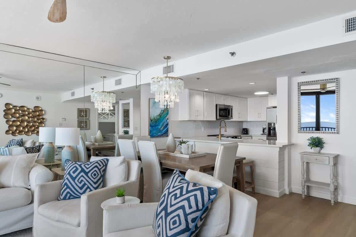 A modern kitchen with white cabinets, a central island, and a dining area with white chairs.