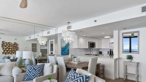 Una cocina moderna con armarios blancos, una isla central y un área de comedor con sillas blancas.