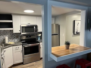 A modern kitchen with white cabinets, a stainless steel oven, a microwave, and a refrigerator.