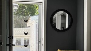 Eine offene Tür, die zu einer Veranda mit einem Stuhl und einem runden Spiegel an der Wand führt.