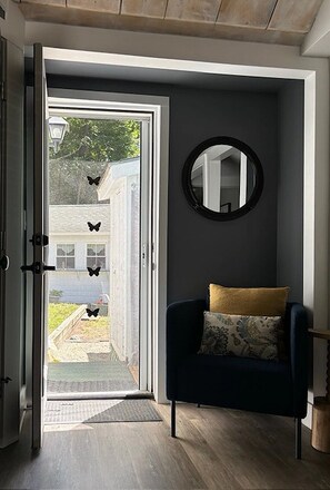 An open door leading to a porch with a chair and a round mirror on the wall.
