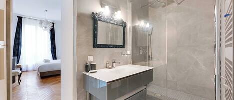 A modern bathroom with a glass shower enclosure, a large mirror, and a vanity with a white sink.