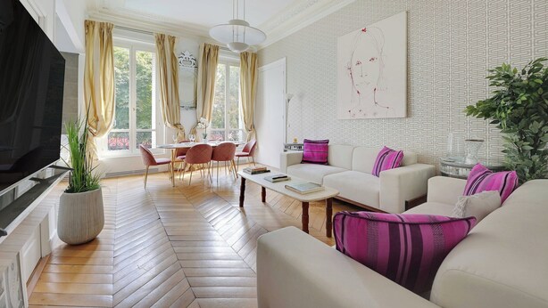 Een ruime woonkamer met een grote televisie, een eethoek met stoelen, een bank met kussens en een groot raam met gordijnen.