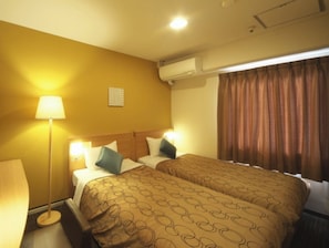 Ein Hotelzimmer mit zwei Betten, einer Lampe, einer Klimaanlage und einem Fenster mit Vorhängen.