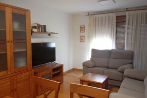 A living room with a flat-screen TV, wooden furniture, a grey sofa, and a window with curtains. - 24B03 Apartamento espacioso en Arenas de Cabrales (Cabrales)