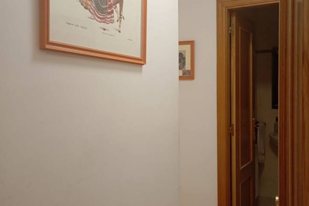 Een hal met kunstwerken in lijsten aan de muur, een houten deur en een kijkje in een badkamer.