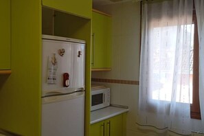 A kitchen with a white refrigerator, a microwave, and a window with a curtain. - 24B03 Apartamento espacioso en Arenas de Cabrales (Cabrales)