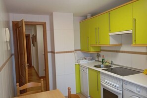 A compact kitchen with green cabinets, a dishwasher, a stove, and a sink. - 24B03 Apartamento espacioso en Arenas de Cabrales (Cabrales)