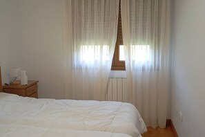 A bedroom with a bed, a nightstand, a window with sheer curtains, and a radiator. - 24B03 Apartamento espacioso en Arenas de Cabrales (Cabrales)