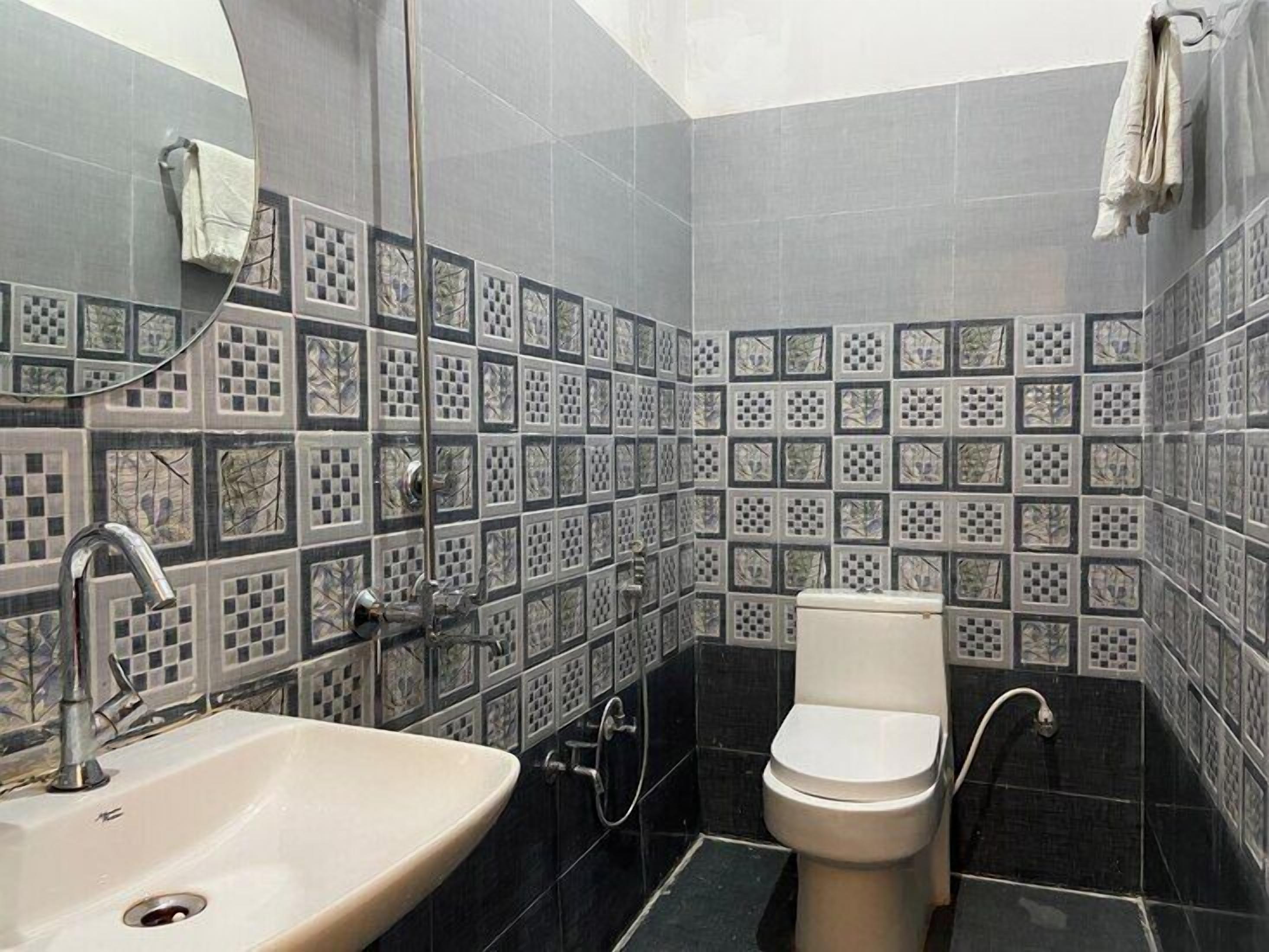 A bathroom with a sink, toilet, and shower. The walls are tiled with a geometric pattern.