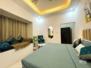 Un dormitorio moderno con una cama grande, una zona de estar con sofá y sillón, una planta en maceta y un espejo.