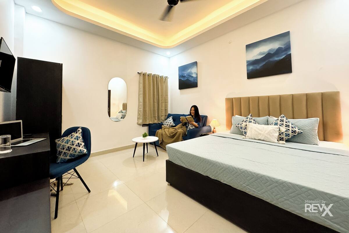 A modern hotel room with a bed, a desk, a chair, a small table, and a ceiling fan.