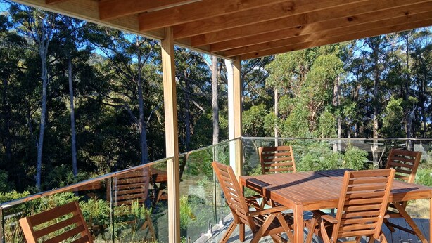 A wooden deck with a glass railing, a table, and chairs. - cosy cottage with wood heater, surrounded by bushland (Middleton)
