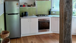 A kitchen with a stainless steel refrigerator, a gas stove, and a built-in oven. There are white cabinets and a green backsplash. - cosy cottage with wood heater, surrounded by bushland (Middleton)