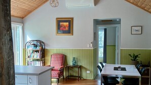 A spacious room with a high wooden ceiling, a dining table with chairs, a red patterned chair, a bookshelf, and a framed picture on the wall. - cosy cottage with wood heater, surrounded by bushland (Middleton)