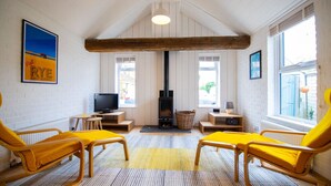 Ein gemütliches Zimmer mit Kamin, Holzbalken, Fernseher und gelben Sesseln.