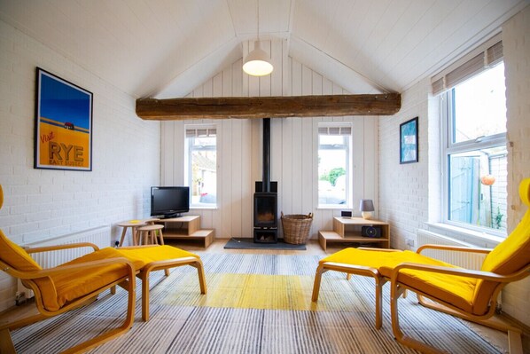 A cozy room with a fireplace, wooden beams, a TV, and yellow chairs. - The Dees - Cottage, Rye Harbour (Rye Harbour)