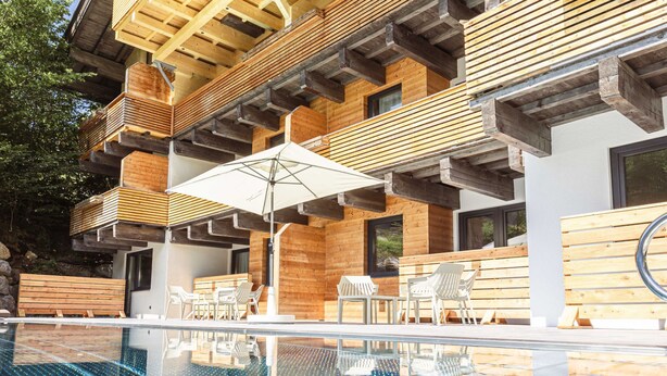 A modern outdoor pool area with wooden deck seating and a glass-enclosed pool. - Premium Suite mit 2 SZ & Mini-Spa by Interhome (Saalbach-Hinterglemm)