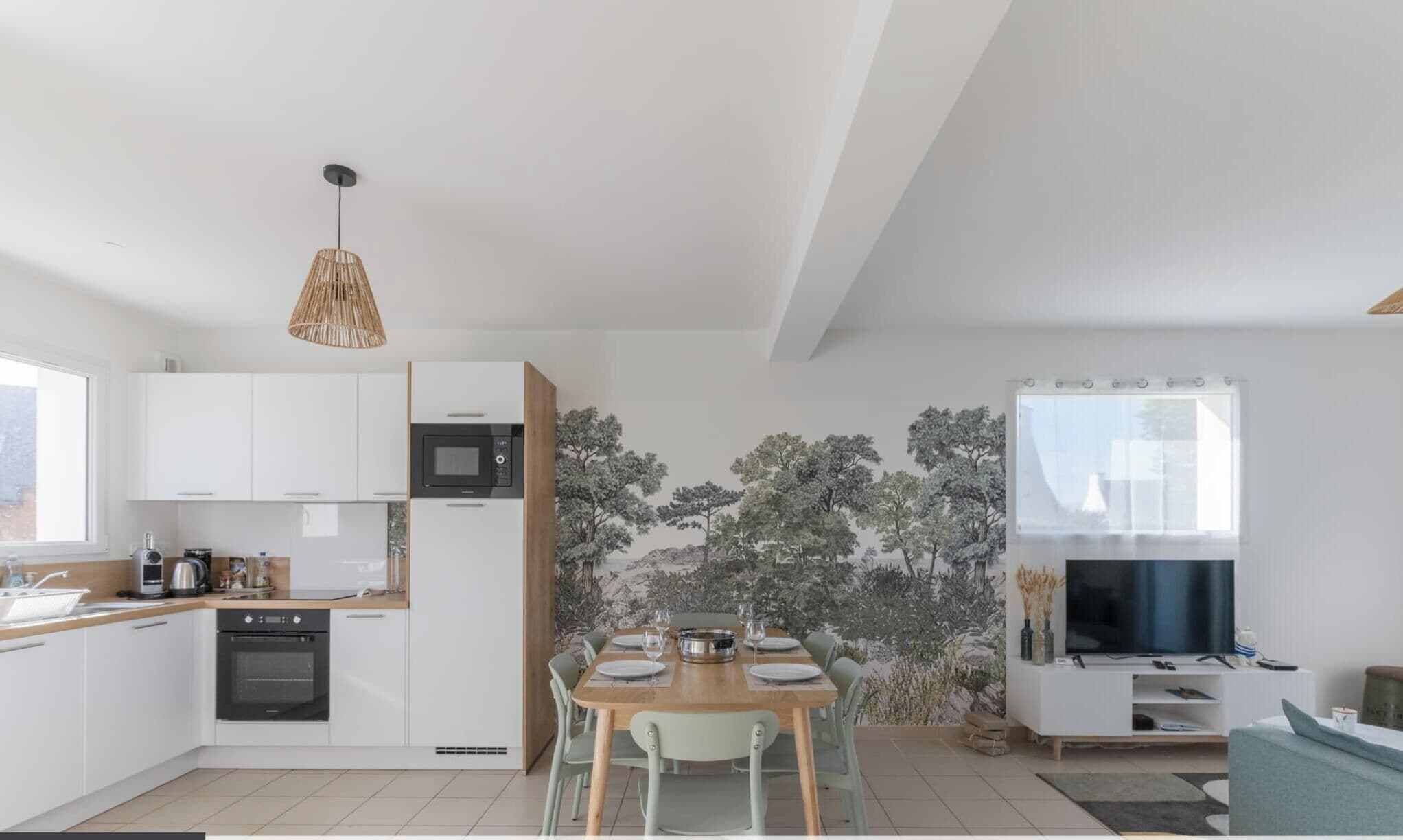 A modern kitchen with white cabinets, a dining table set for four, a TV, and a large window.