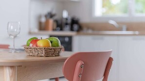 A kitchen with a wooden table, a wicker fruit basket, and a pink chair.