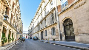 Rua com edifícios históricos, céu claro e alguns carros estacionados.